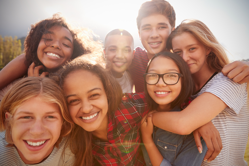 a group of youths post for a selfie, smiling, with arms around one another