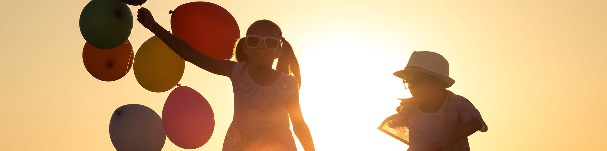 two children holding balloons in sunset