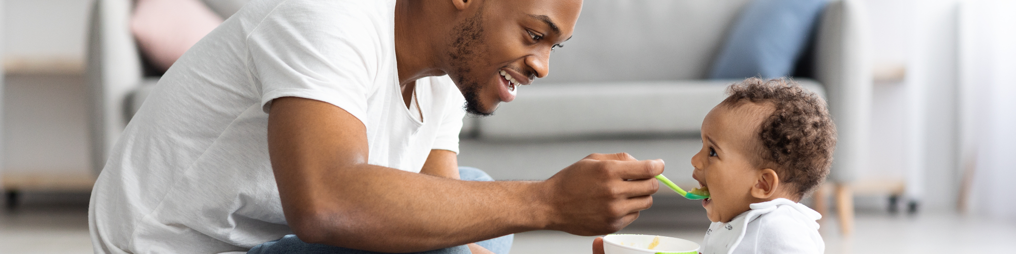 smiling African American father feeding baby with spoon